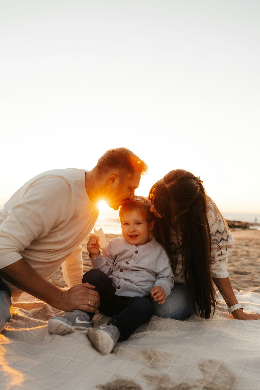 Parents kissing their toddler on a beach blanket