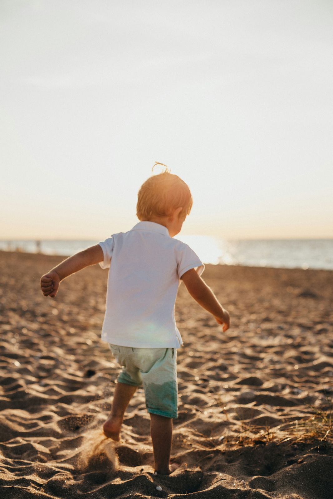 Toddler kicking up sand at sunset