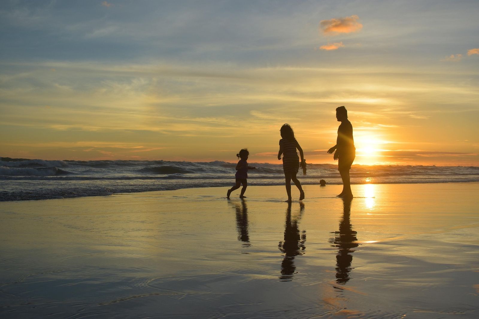 Dad and two kids playing at the water's edge at sunset