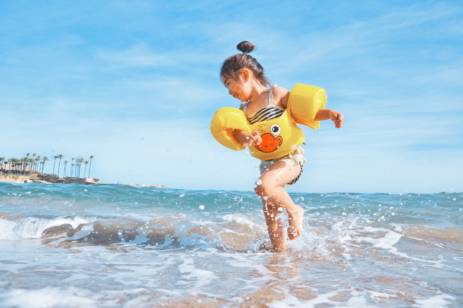 Little girl in a duck swim vest splashing in the waves