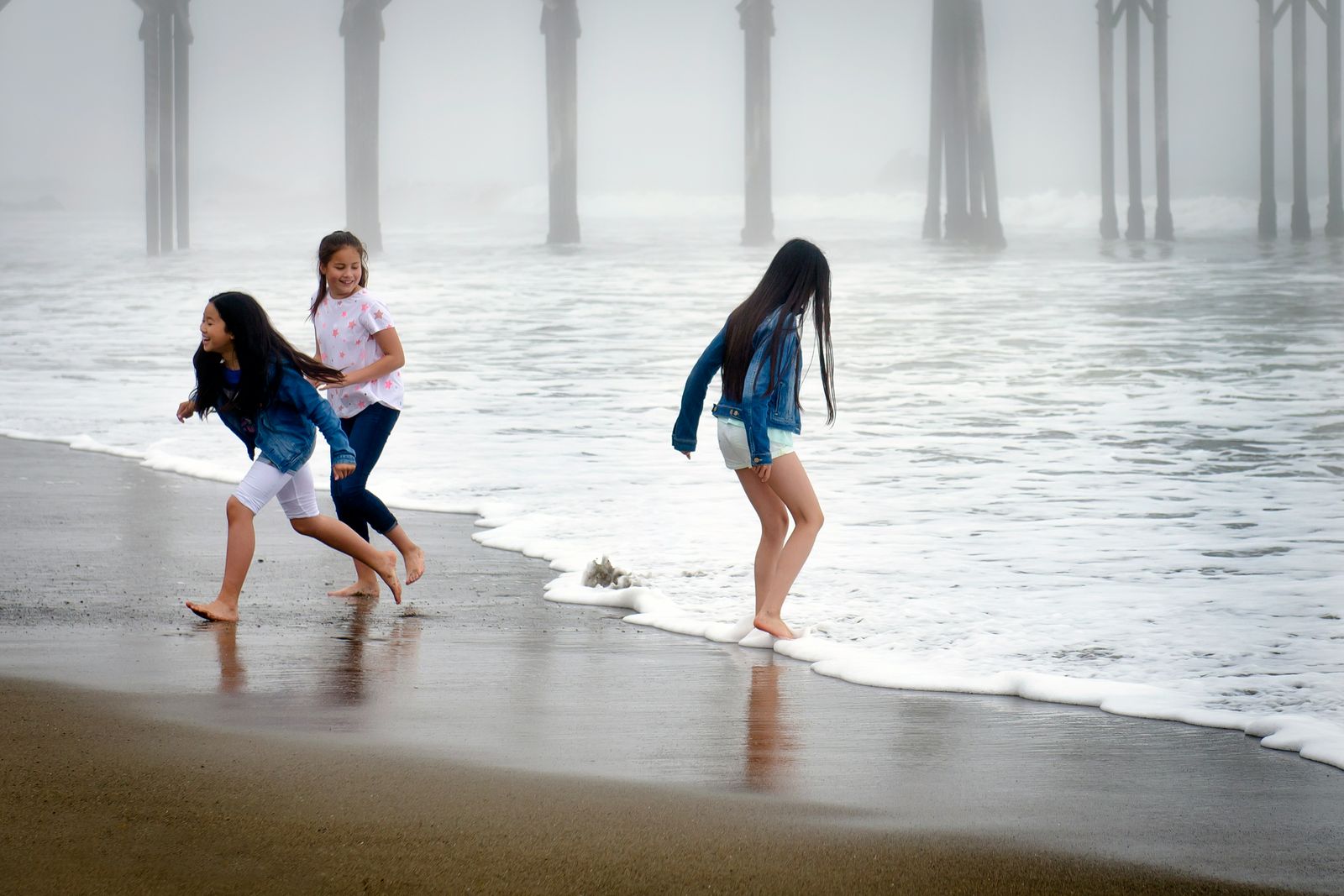 Three girls racing the waves on a foggy morning