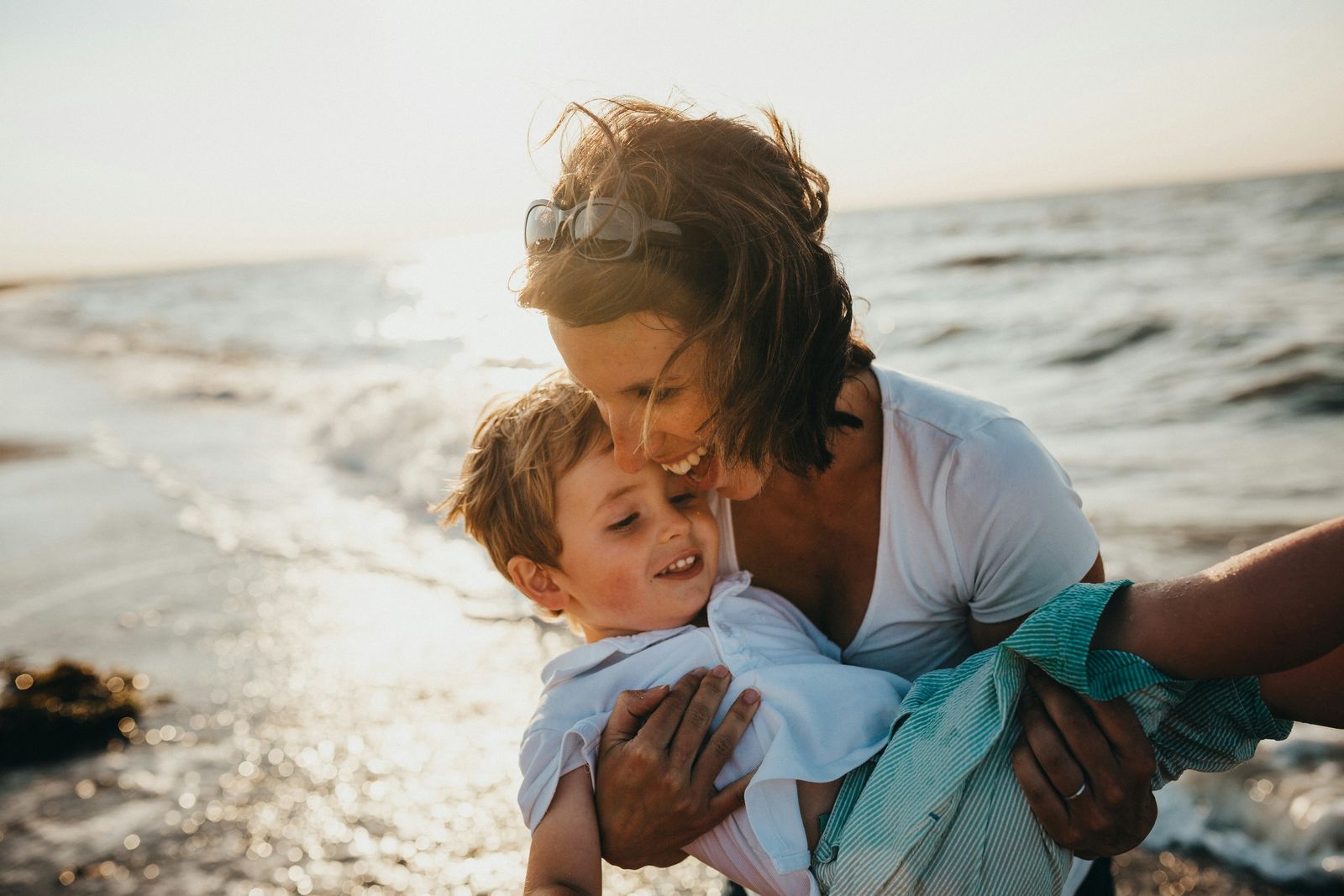 Mom laughing as she scoops up her son by the water