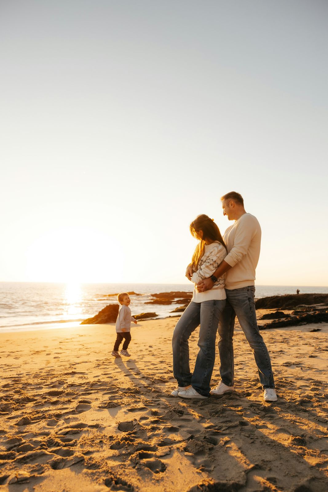 Couple hugging while their son runs on the sand
