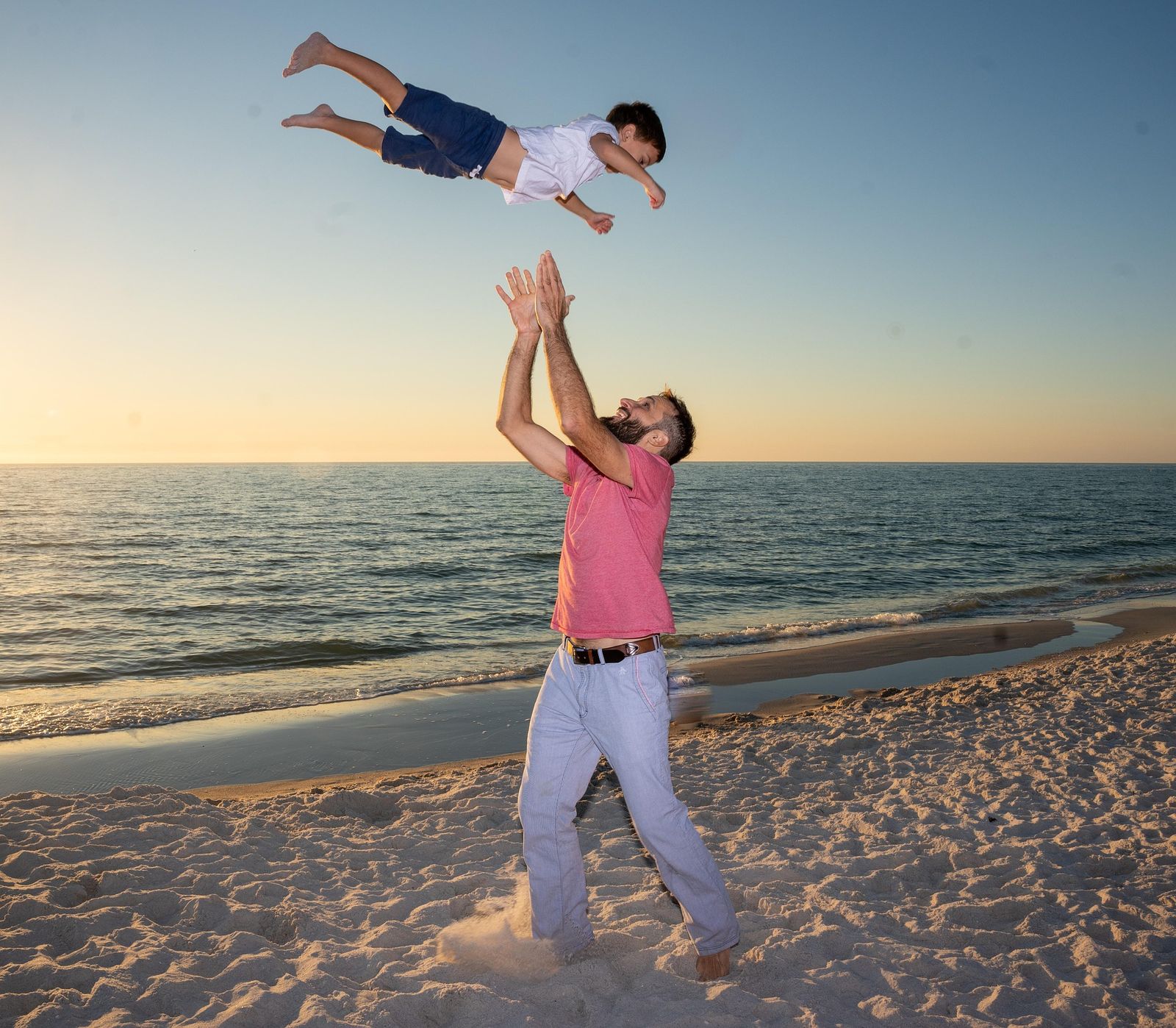 Dad tossing his son into the air on the beach